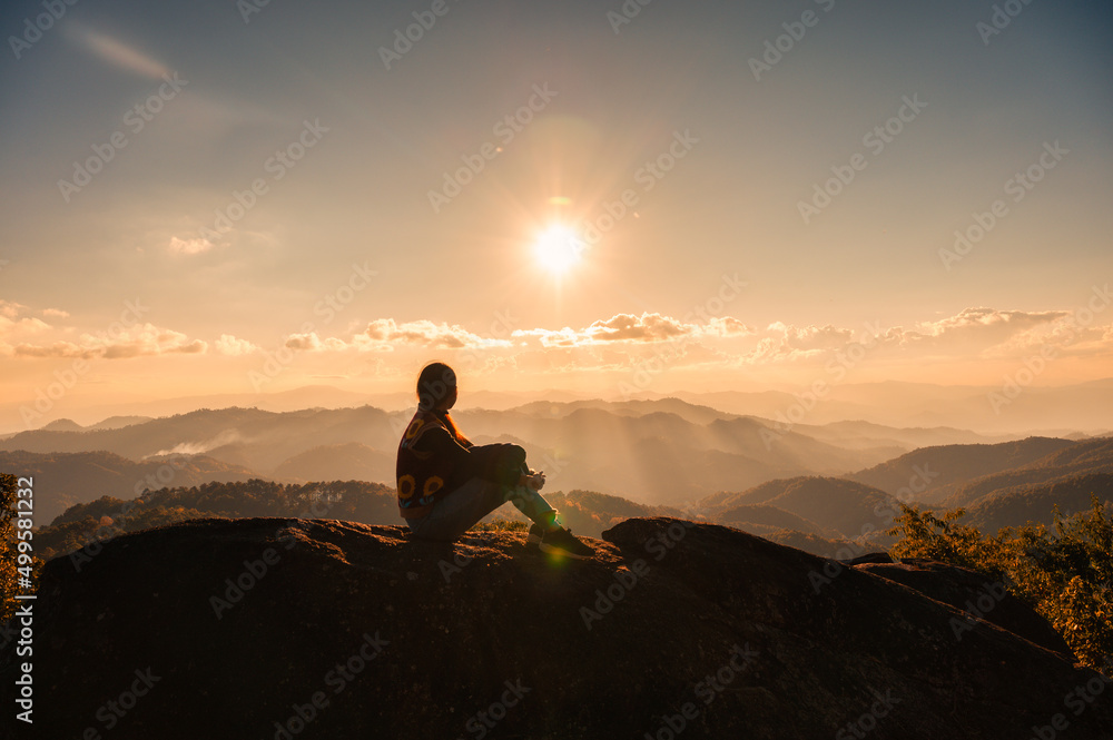 Silhouette young hiker woman relaxing and enjoying the sunset view on top of mountain peak at national park
