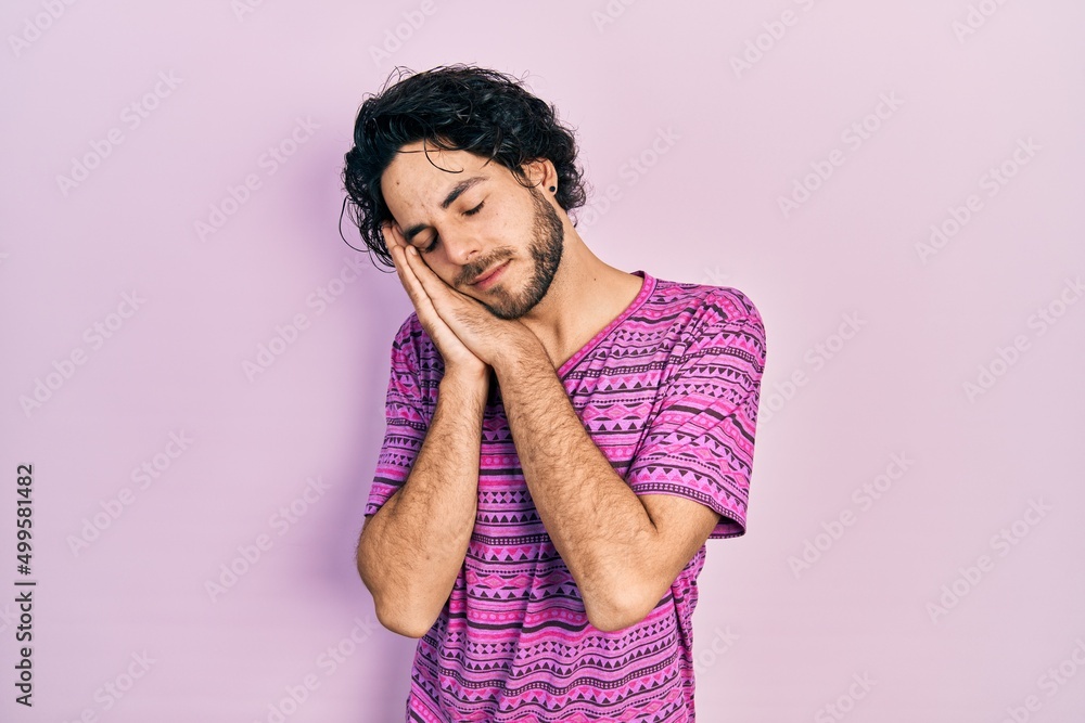 Handsome hispanic man wearing casual pink t shirt sleeping tired dreaming and posing with hands together while smiling with closed eyes. Handsome hispanic man wearing casual pink t shirt sleeping tired dreaming and posing with hands together while smiling with closed eyes.