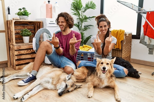 Photography Young hispanic couple doing laundry with dogs showing middle finger doing fuck you bad expression, provocation and rude attitude