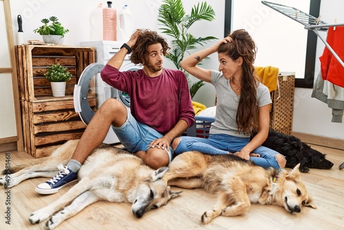 Canvas Print Young hispanic couple doing laundry with dogs confuse and wondering about question