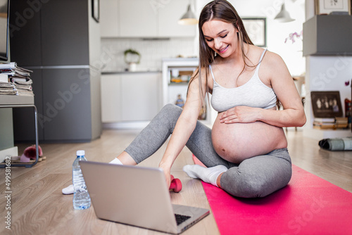 Pregnant woman exercising on yoga mat in living room at home.