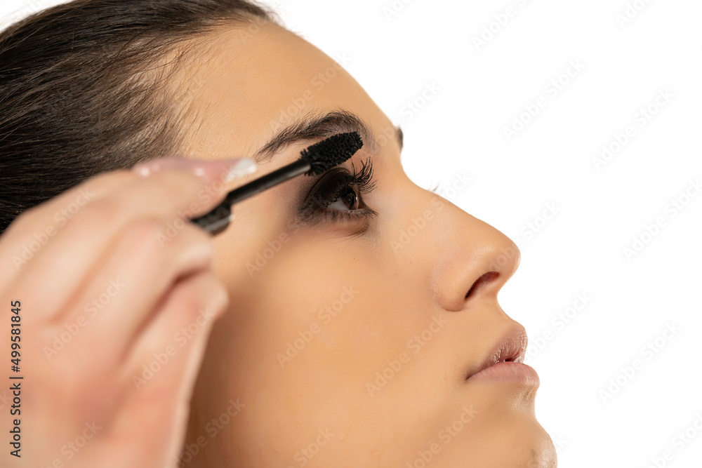 Close up of woman applying mascara on the lower eyelashes on a white background