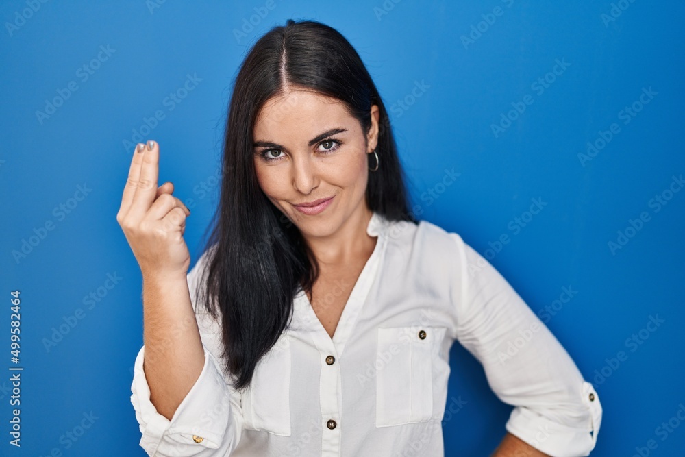 Young hispanic woman standing over blue background doing italian gesture with hand and fingers confident expression Young hispanic woman standing over blue background doing italian gesture with hand and fingers confident expression