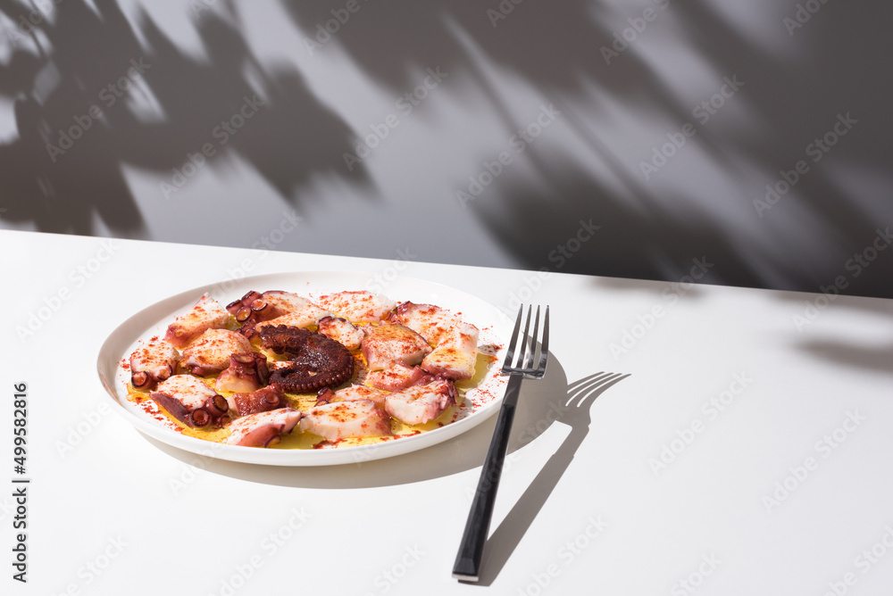 Plato de pulpo a la gallega con pimentón y aceite de oliva. Tapa típica española sobre mesa blanca