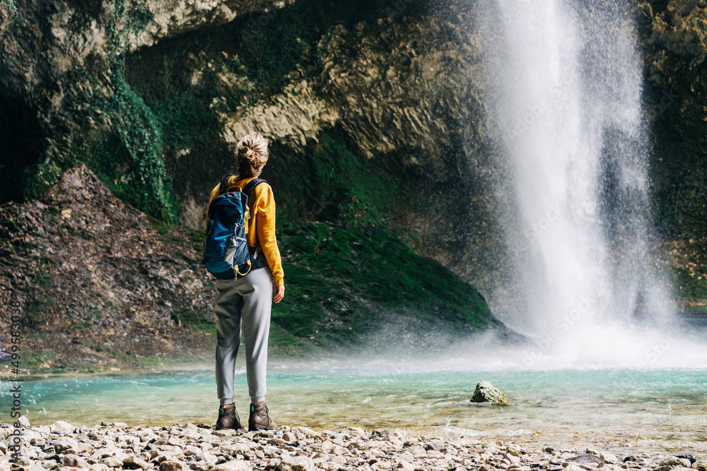 Woman tourist with a backpack on an expedition in the canyon looks at the waterfall