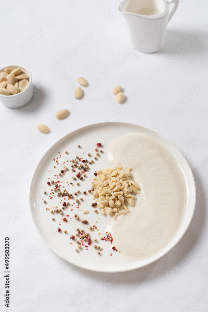 Crema de almendras, sopa fría española. Ajo blanco de Málaga con almendras en un recipiente blanco sobre una mesa blanca. Vista superior Crema de almendras, sopa fría española. Ajo blanco de Málaga con almendras en un recipiente blanco sobre una mesa blanca. Vista superior