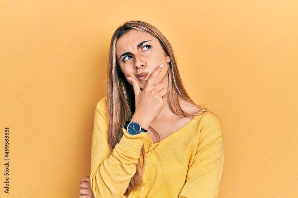 Beautiful hispanic woman wearing casual yellow sweater thinking worried about a question, concerned and nervous with hand on chin Beautiful hispanic woman wearing casual yellow sweater thinking worried about a question, concerned and nervous with hand on chin