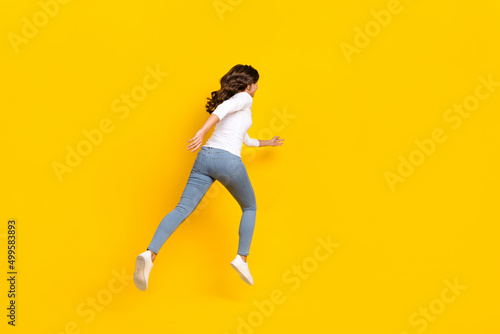 Photo of pretty excited lady dressed white shirt running fast jumping high isolated yellow color background © deagreez