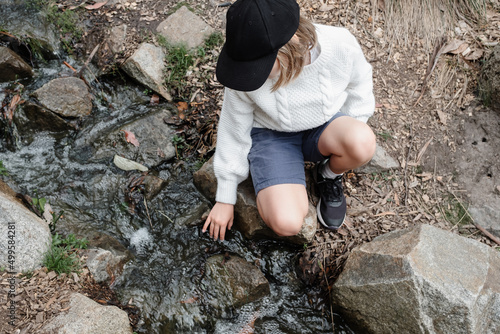 Young girl sitting by a creek touching the water