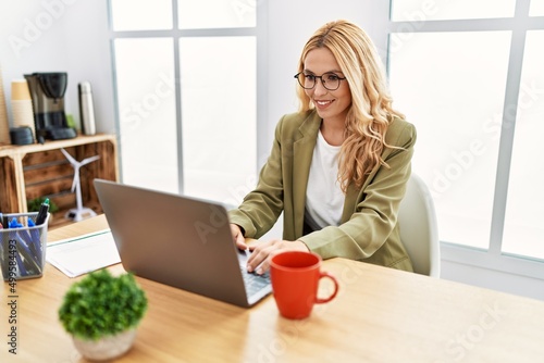 Beautiful blonde woman working at the office with laptop with a happy and cool smile on face. lucky person.