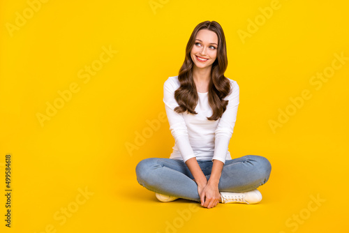 Photo of cute dreamy lady dressed white shirt sitting legs crossed looking empty space isolated yellow color background