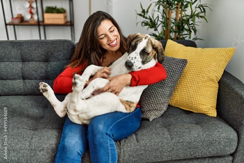 Young woman hugging dog sitting on sofa at home