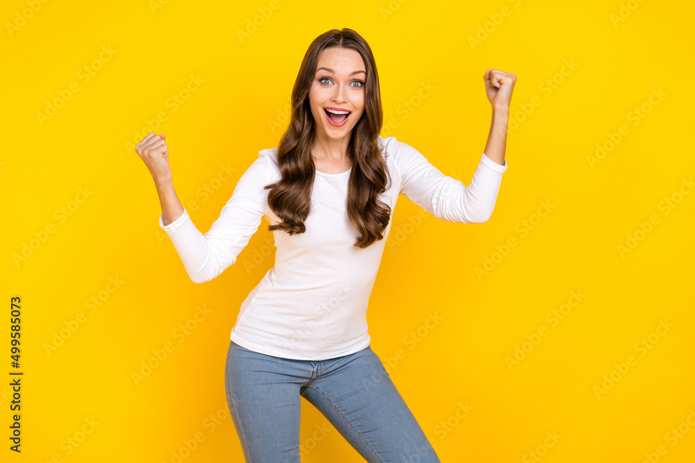 Photo of sweet lucky woman wear white shirt smiling rising fists isolated yellow color background Photo of sweet lucky woman wear white shirt smiling rising fists isolated yellow color background