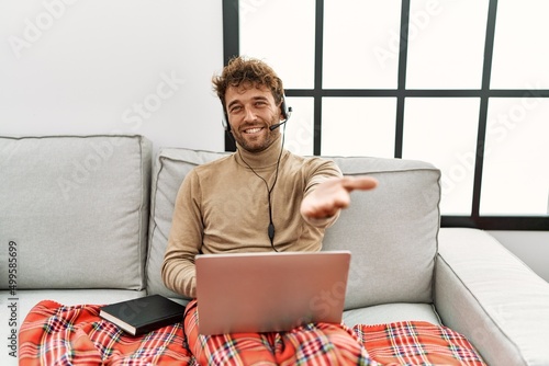 Young handsome man with beard wearing operator headset working from home smiling cheerful offering palm hand giving assistance and acceptance.