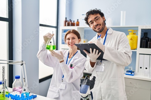 Man and woman scientist partners holding test tube writing on clipboard at laboratory