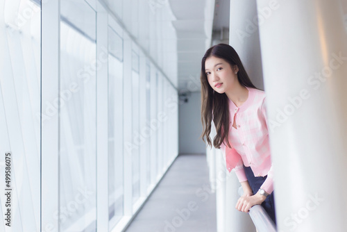 Beautiful teenage Asian girl wears a white with pink shirt and smiles cheerfully while she stands near the glassed window on a nice day. Free Download Beautiful teenage Asian girl wears a white with pink shirt and smiles cheerfully while she stands near the glassed window on a nice day. - GFXLoad