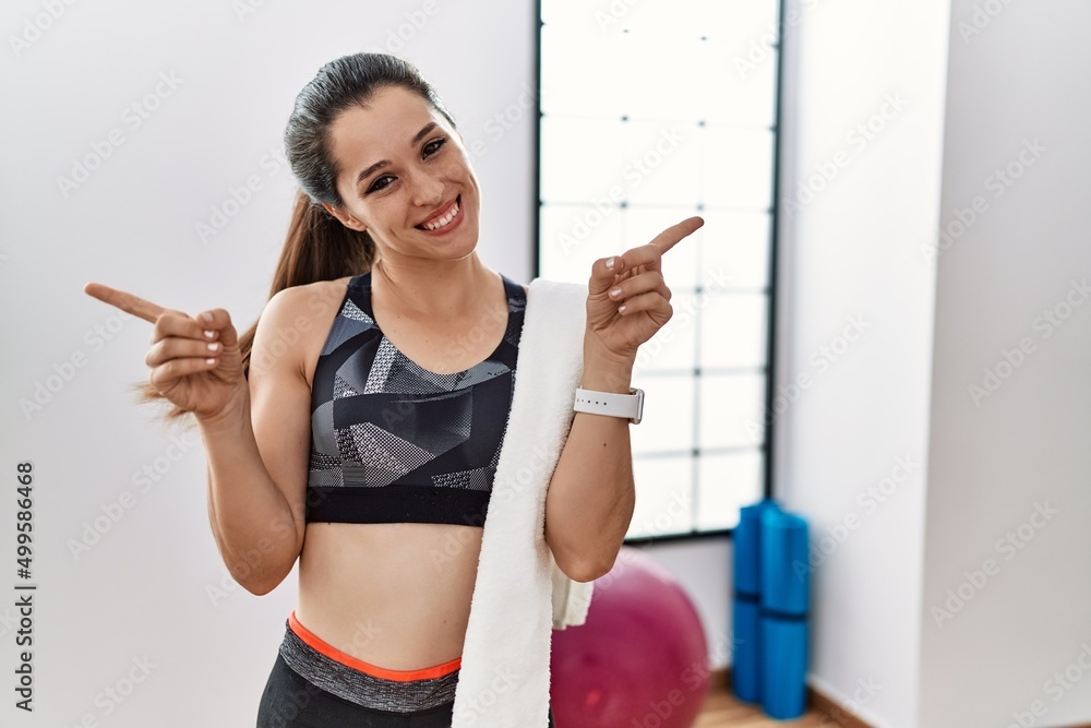 Young brunette woman wearing sportswear and towel at the gym smiling confident pointing with fingers to different directions. copy space for advertisement Young brunette woman wearing sportswear and towel at the gym smiling confident pointing with fingers to different directions. copy space for advertisement