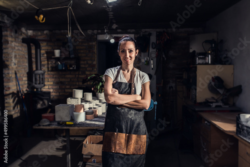 Portrait of craftswoman in apron working in her workshop making decorative concrete vase.