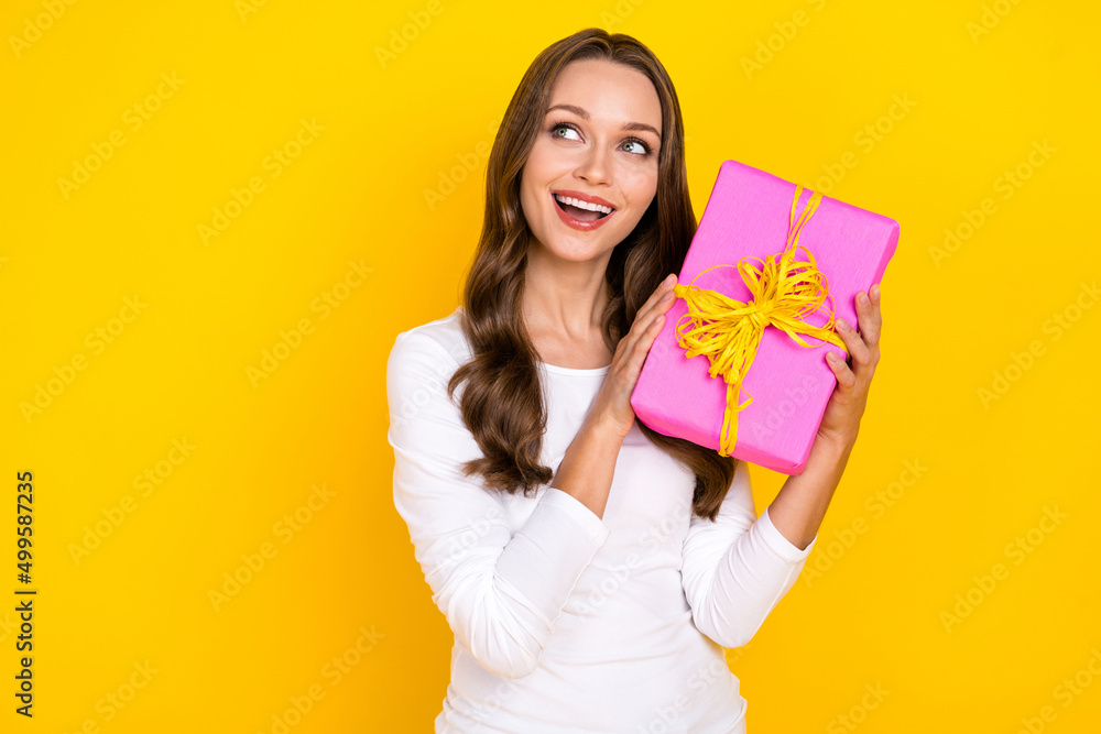 Photo of curious creative lady hold gift look empty space try guess wear white shirt isolated yellow color background Photo of curious creative lady hold gift look empty space try guess wear white shirt isolated yellow color background