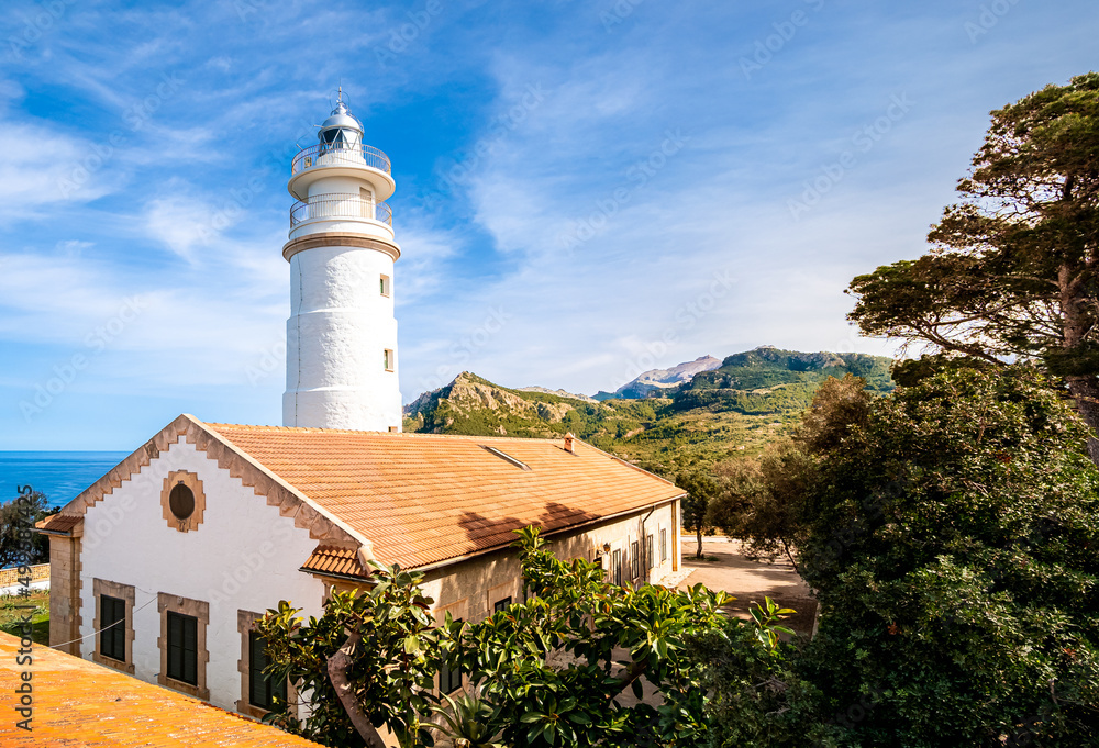 Outside view over the sunlit lighthouse Far del Cap Gros in puerto de soller with the mountain ridge of the serra de tramuntana in the background.