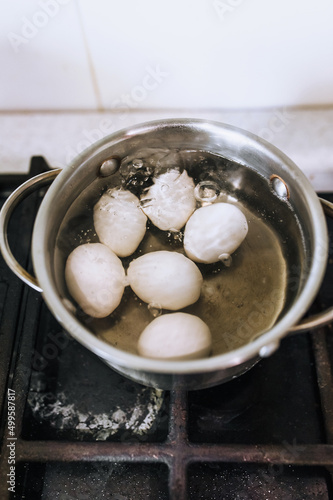 Chicken white eggs are boiled in boiling water in a metal saucepan.