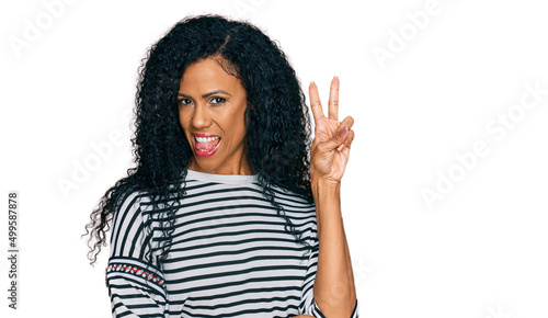 Middle age african american woman wearing casual clothes smiling with happy face winking at the camera doing victory sign. number two.