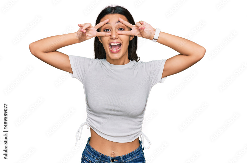 Young hispanic girl wearing casual white t shirt doing peace symbol with fingers over face, smiling cheerful showing victory Young hispanic girl wearing casual white t shirt doing peace symbol with fingers over face, smiling cheerful showing victory