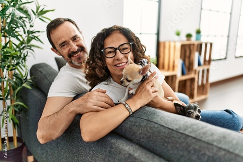 Photography Middle age hispanic couple smiling happy sitting on the sofa with dogs at home