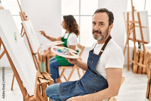 Hispanic middle age man and mature woman at art studio thinking attitude and sober expression looking self confident