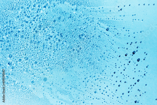 Blue water background with bubbles and drops, flat lay. Abstract clear liquid texture for skincare product backdrop.