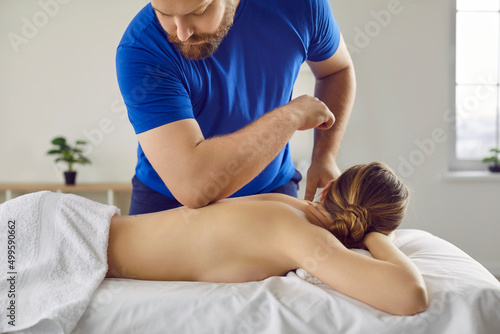 Professional massagist specialist at health center, spa studio, parlor uses elbow for therapeutic remedial shiatsu or Lomi technique spine back massage to help beautiful woman lying on table bed couch