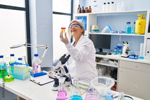 Middle age woman wearing scientist uniform holding urine analysis test tube at laboratory