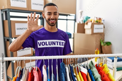 African american man wearing volunteer t shirt at donations stand showing and pointing up with fingers number five while smiling confident and happy.