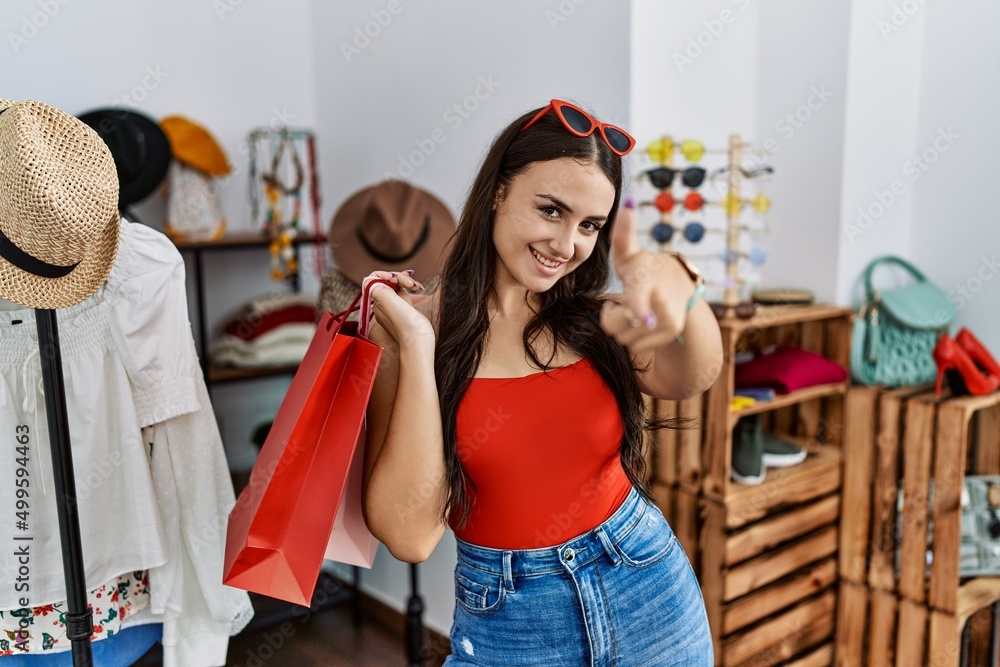 Young brunette woman holding shopping bags at retail shop pointing fingers to camera with happy and funny face. good energy and vibes. Young brunette woman holding shopping bags at retail shop pointing fingers to camera with happy and funny face. good energy and vibes.