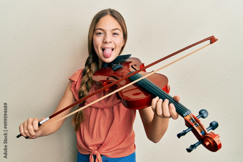 Beautiful brunette little girl playing violin sticking tongue out happy with funny expression. Beautiful brunette little girl playing violin sticking tongue out happy with funny expression.