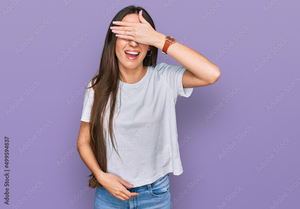 Young hispanic girl wearing casual white t shirt smiling and laughing with hand on face covering eyes for surprise. blind concept. Young hispanic girl wearing casual white t shirt smiling and laughing with hand on face covering eyes for surprise. blind concept.