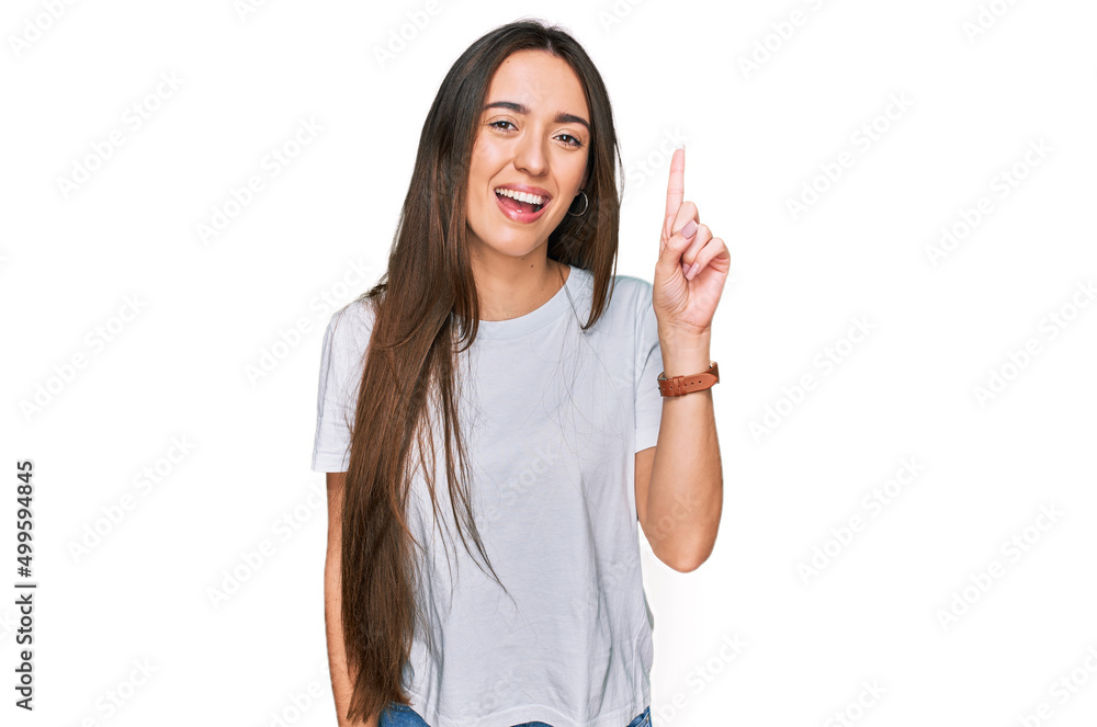 Young hispanic girl wearing casual white t shirt pointing finger up with successful idea. exited and happy. number one. Young hispanic girl wearing casual white t shirt pointing finger up with successful idea. exited and happy. number one.