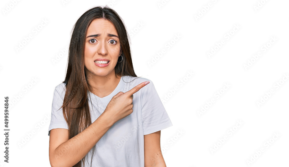 Young hispanic girl wearing casual white t shirt pointing aside worried and nervous with forefinger, concerned and surprised expression Young hispanic girl wearing casual white t shirt pointing aside worried and nervous with forefinger, concerned and surprised expression