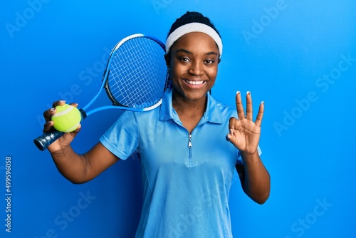 African american woman with braided hair playing tennis holding racket and ball doing ok sign with fingers, smiling friendly gesturing excellent symbol © Krakenimages.com