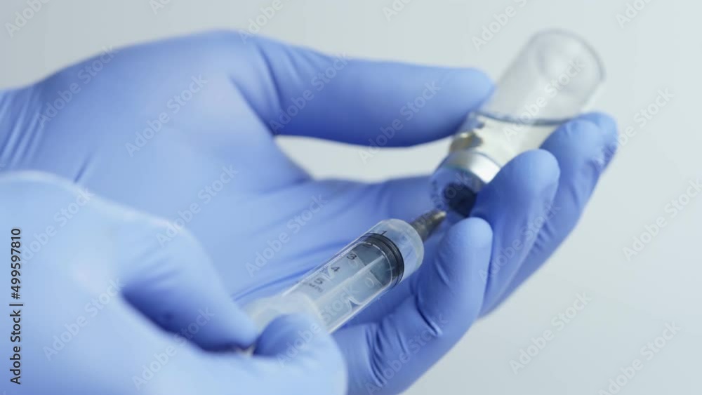 Close-up of Doctor's Hands in Blue Medical Gloves Filling Syringe with Liquid Medication from Glass Vial Close-up of Doctor's Hands in Blue Medical Gloves Filling Syringe with Liquid Medication from Glass Vial