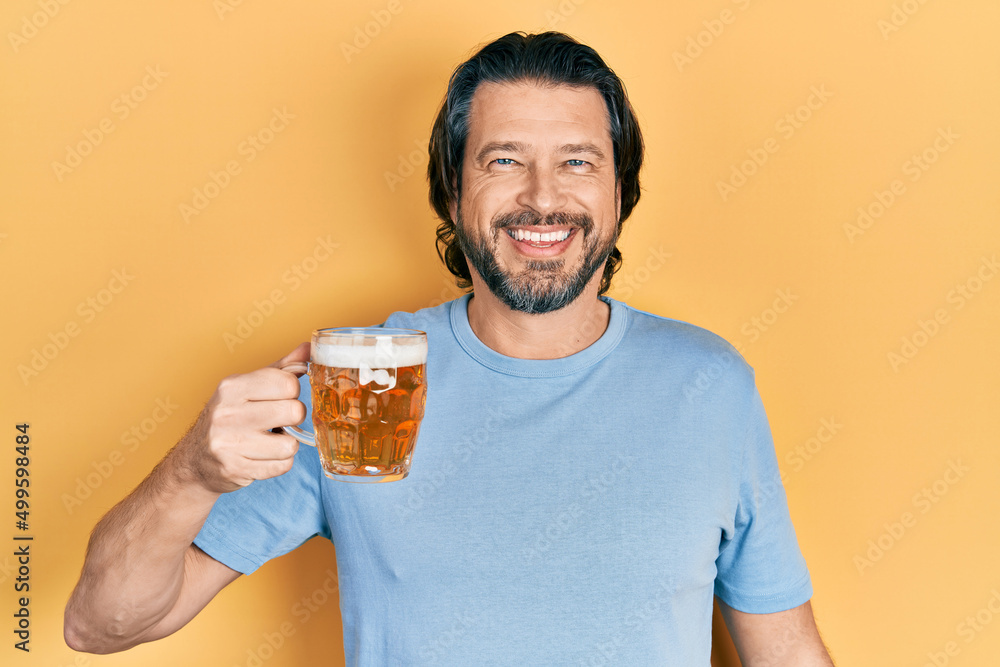 Middle age caucasian man drinking a jar of beer looking positive and happy standing and smiling with a confident smile showing teeth Middle age caucasian man drinking a jar of beer looking positive and happy standing and smiling with a confident smile showing teeth