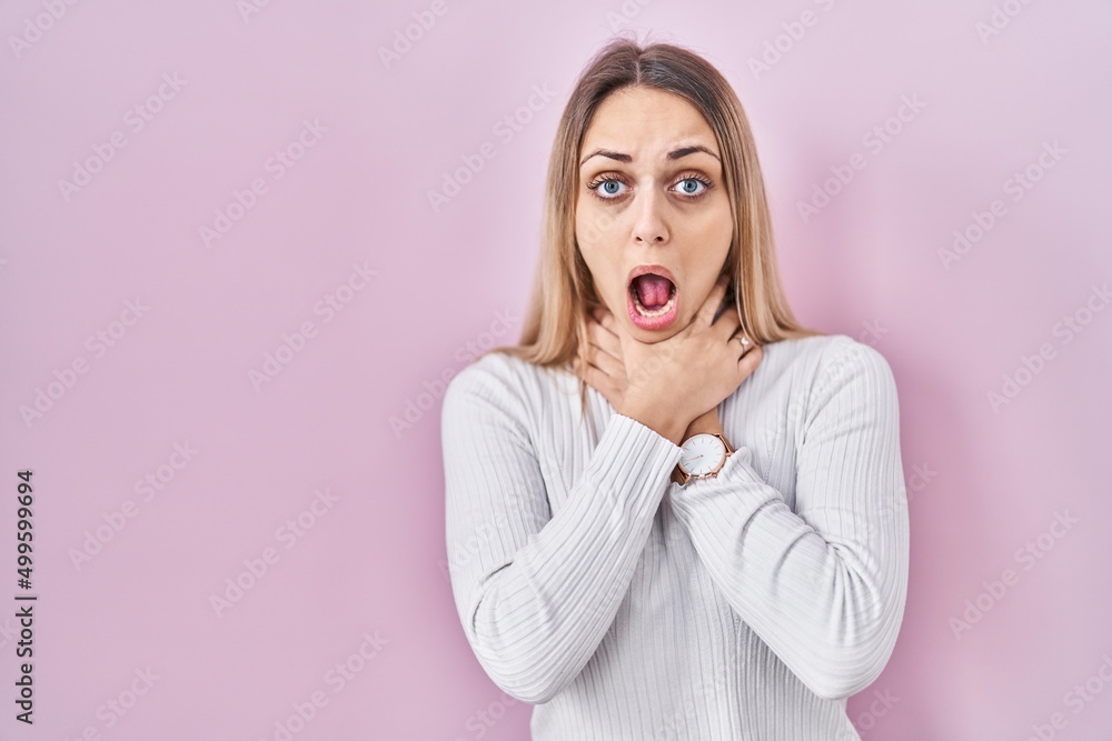 Young blonde woman wearing white sweater over pink background shouting and suffocate because painful strangle. health problem. asphyxiate and suicide concept. Young blonde woman wearing white sweater over pink background shouting and suffocate because painful strangle. health problem. asphyxiate and suicide concept.