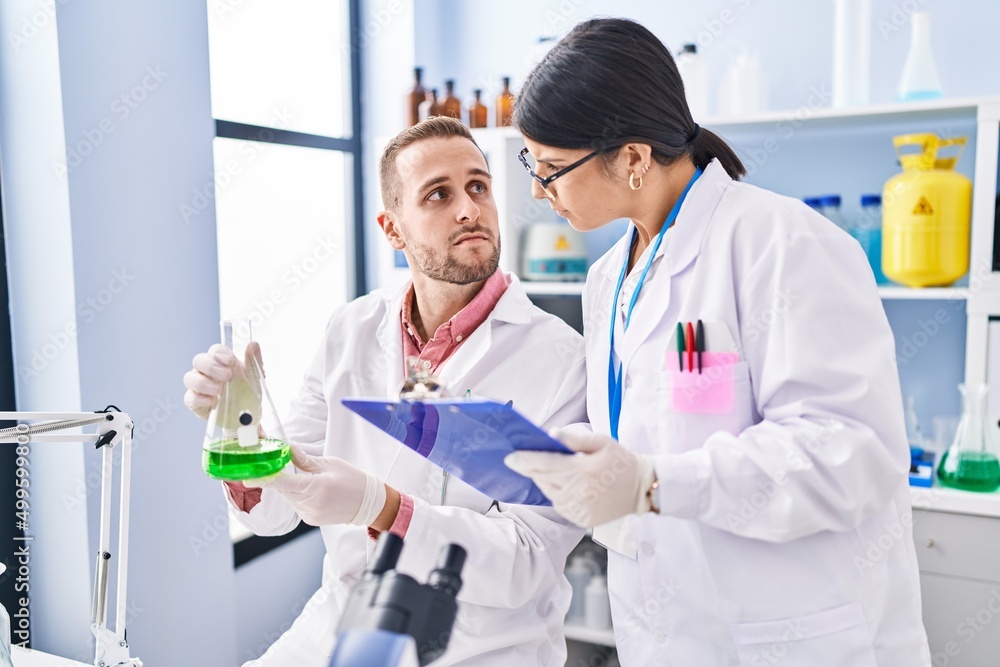 Fototapeta premium Man and woman wearing scientists uniform measuring liquid at laboratory