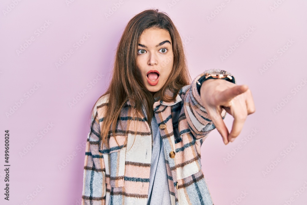 Young caucasian girl wearing casual clothes pointing with finger surprised ahead, open mouth amazed expression, something on the front Young caucasian girl wearing casual clothes pointing with finger surprised ahead, open mouth amazed expression, something on the front