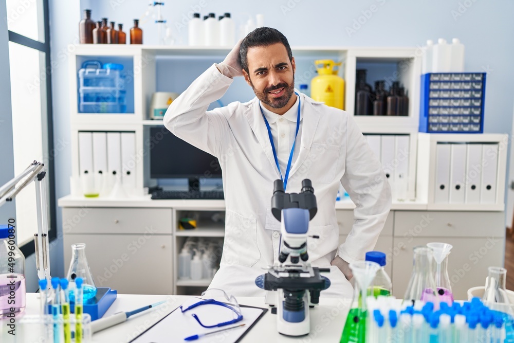 Young hispanic man with beard working at scientist laboratory confuse and wonder about question. uncertain with doubt, thinking with hand on head. pensive concept. Young hispanic man with beard working at scientist laboratory confuse and wonder about question. uncertain with doubt, thinking with hand on head. pensive concept.