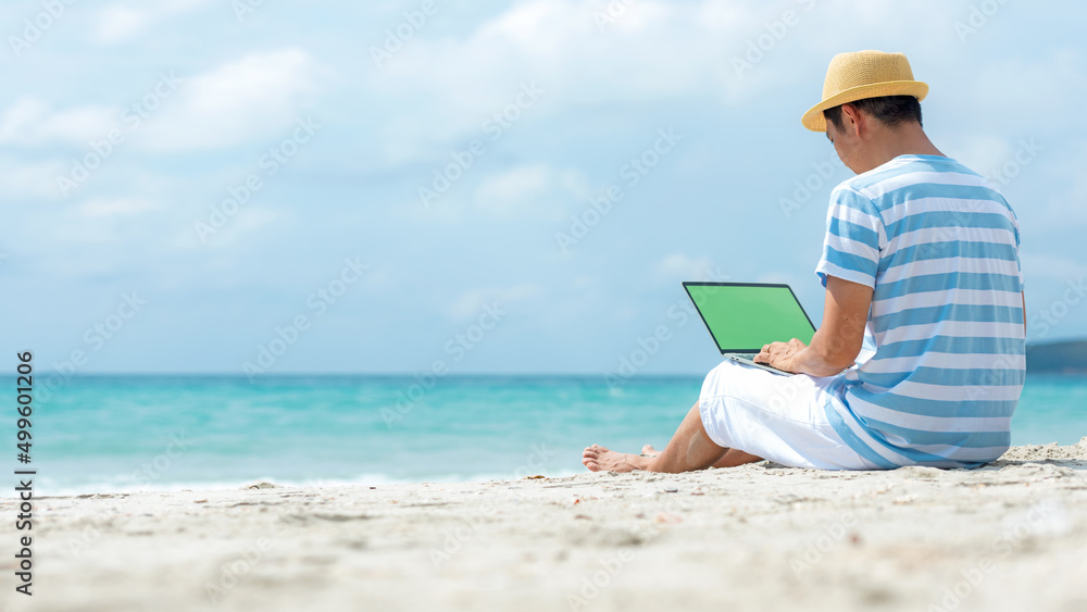 Lifestyle young asian man working on laptop while sitting chill on the beautiful outdoor beach, freelance working social on holiday summer. Summer and Vacation Concept