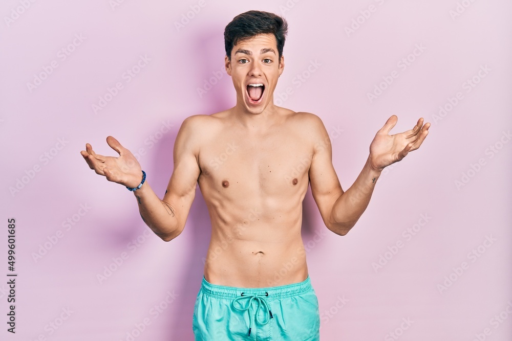Young hispanic man wearing swimwear shirtless celebrating crazy and amazed for success with arms raised and open eyes screaming excited. winner concept