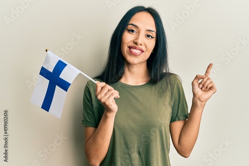 Εκτύπωση καμβά Young hispanic girl holding finland flag smiling happy pointing with hand and fi