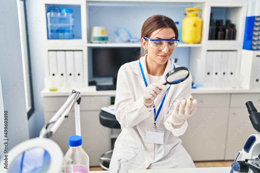 Young hispanic woman wearing scientist uniform using magnifying glass at laboratory Young hispanic woman wearing scientist uniform using magnifying glass at laboratory