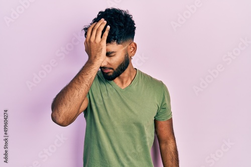 Arab man with beard wearing casual green t shirt surprised with hand on head for mistake, remember error. forgot, bad memory concept.